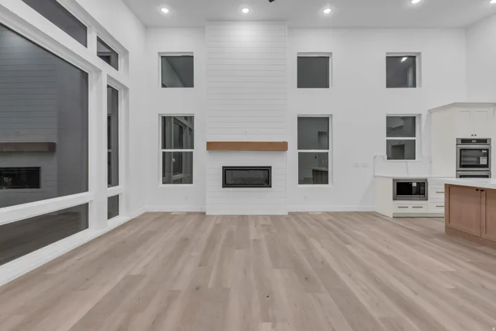 High ceilings with recessed lighting, wood-finish flooring, a contemporary fireplace with a wood mantle, white shaker cabinetry, and built-in stainless steel appliances