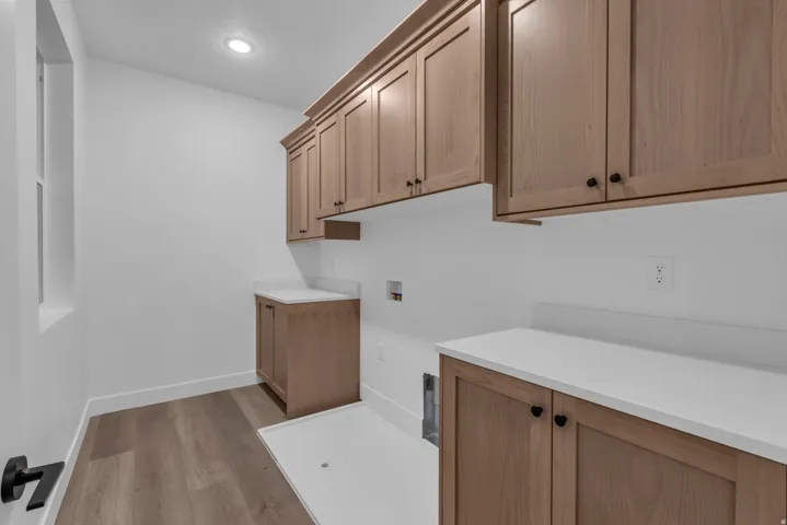 Light wood-finish cabinetry, white solid surface countertops, wood-finish flooring, and a window