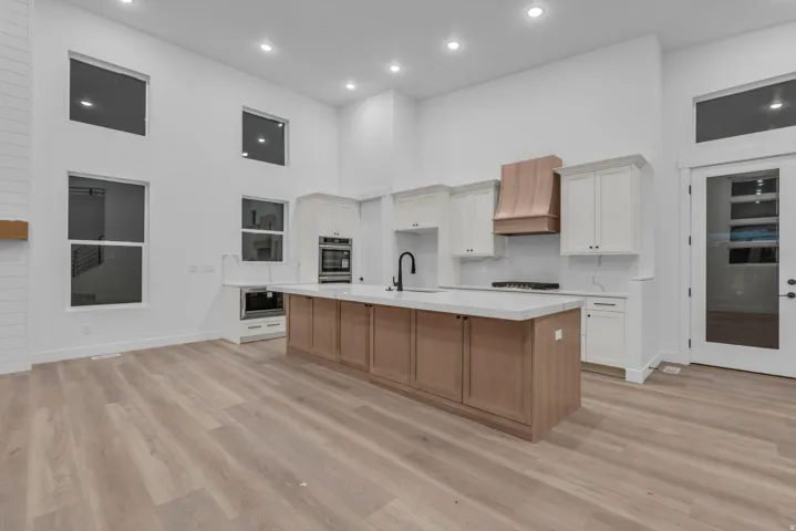 Kitchen featuring a large island with a light-toned countertop, wood-finish flooring, white cabinetry, and a copper-toned range hood