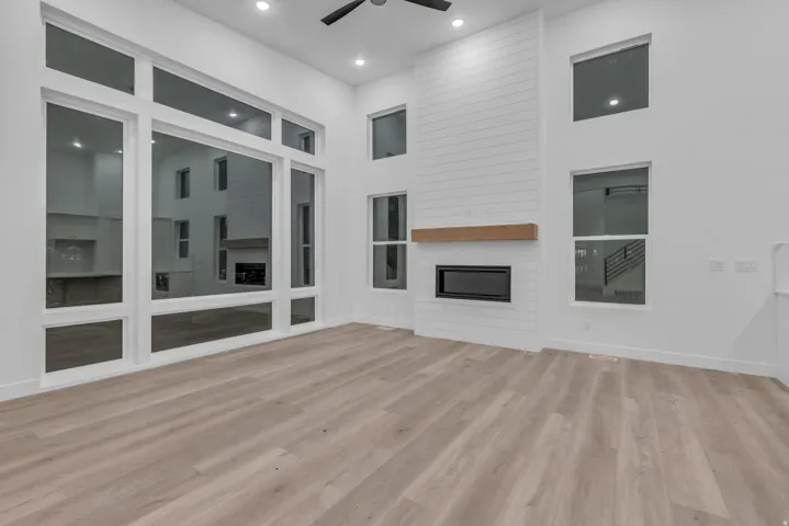 Expansive window wall, high ceilings with recessed lighting, shiplap-style fireplace surround, wood mantel, and wood-finish flooring