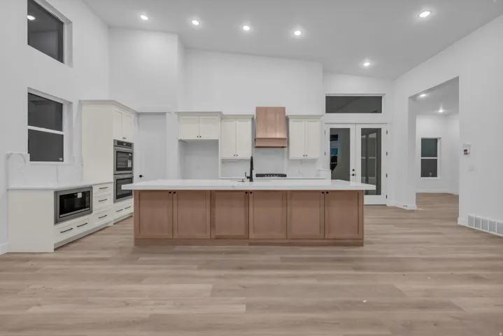 Vaulted ceilings with recessed lighting, two-tone cabinetry with contrasting wood finishes, wood-finish flooring, and a central island with an integrated sink