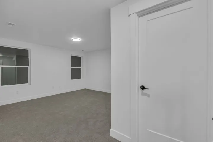 Grey carpeted flooring, white walls, two windows, and a recessed ceiling light