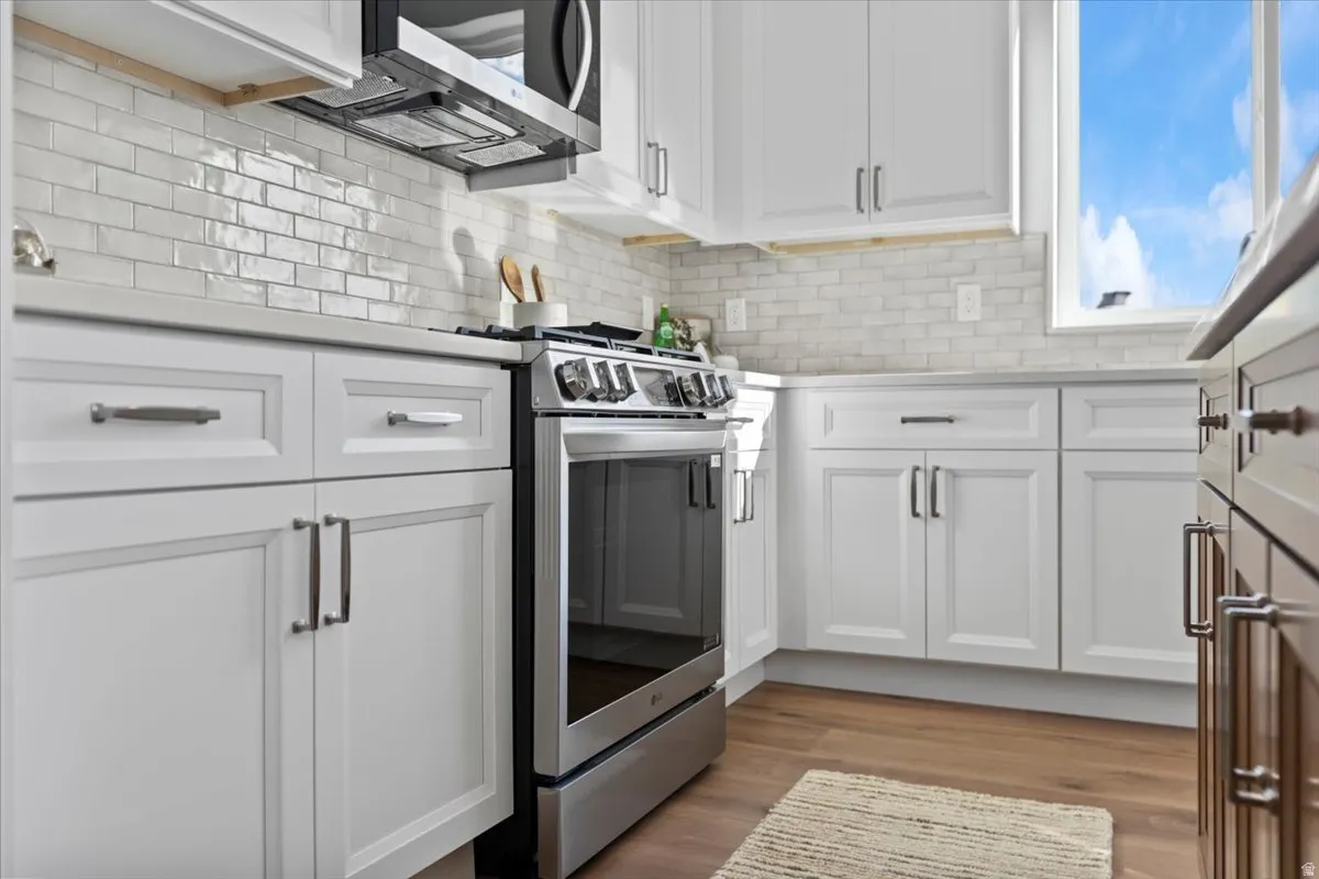 White shaker cabinetry with dark hardware, stainless steel range and microwave, subway tile backsplash, and light-toned countertops