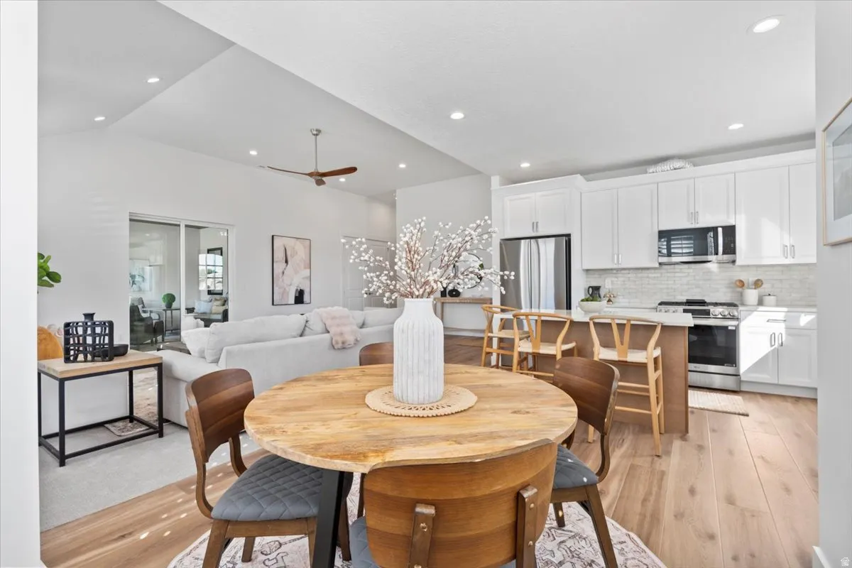 Vaulted ceilings, wood-finish flooring, white shaker cabinetry, stainless steel appliances, and a kitchen island with seating