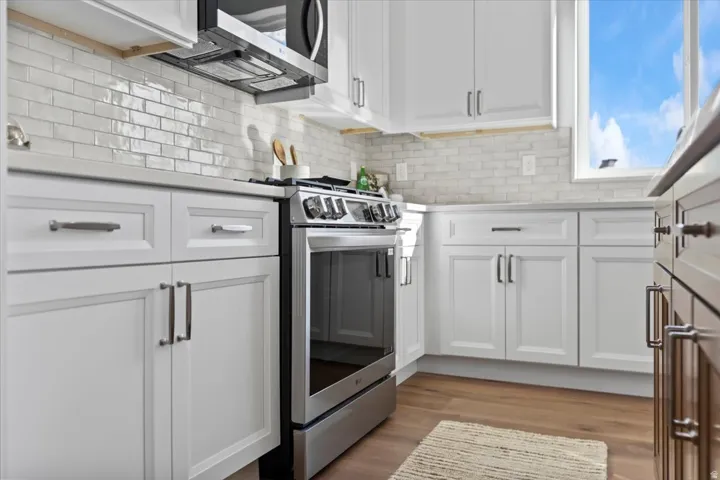 White shaker cabinetry with dark hardware, stainless steel range and microwave, subway tile backsplash, and light-toned countertops