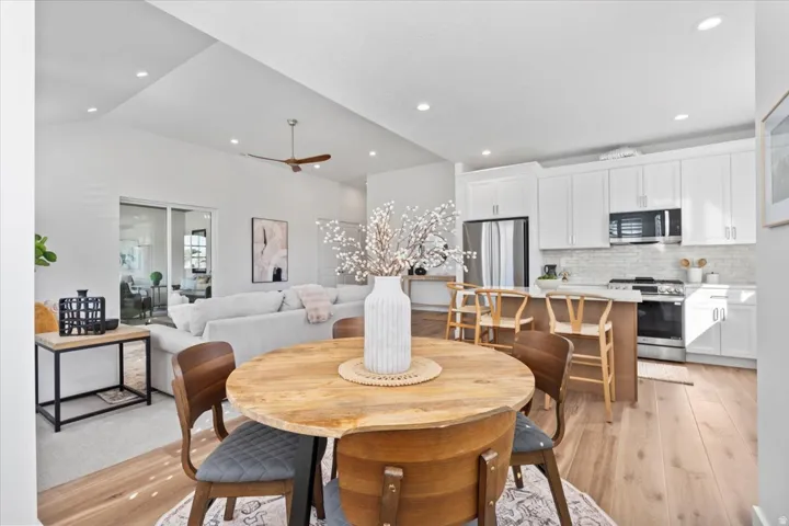 Vaulted ceilings, wood-finish flooring, white shaker cabinetry, stainless steel appliances, and a kitchen island with seating