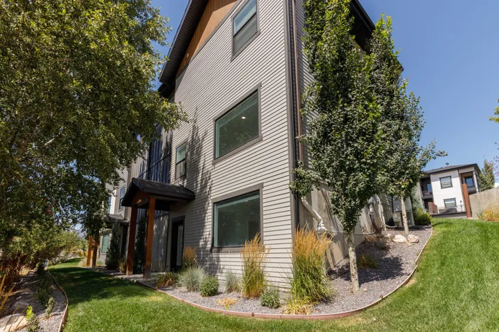 Modern exterior featuring horizontal siding, dark trim, a covered entry with wood posts, and a landscaped yard with mature trees and groundcover