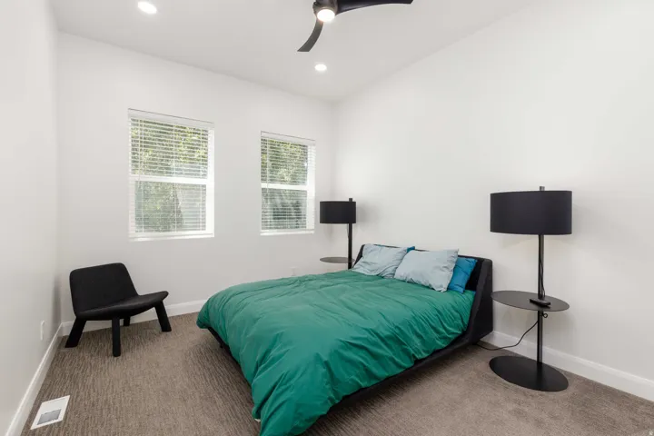 Recessed lighting, ceiling fan, two windows with blinds, and neutral carpeting
