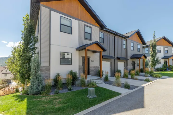 Modern townhome exterior with mixed material siding, natural wood accents, covered entryways, and integrated garage doors