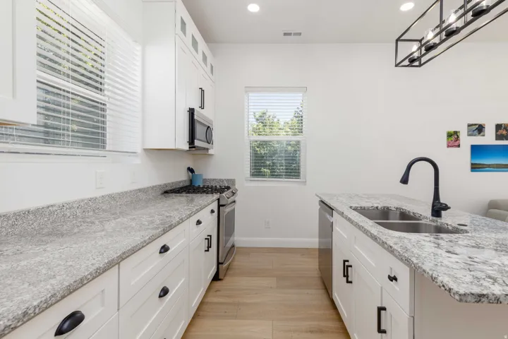 White cabinetry with black hardware, granite countertops, stainless steel appliances, wood-finish flooring, and a black gooseneck faucet