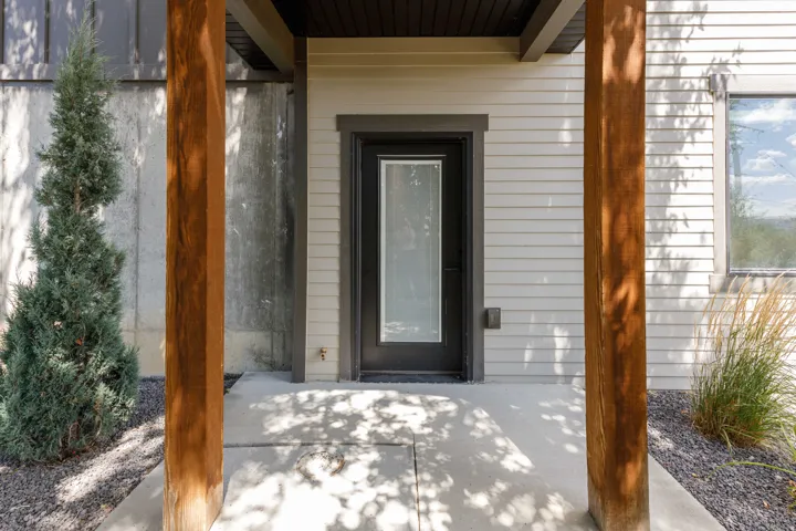 Covered entry with wood-finish support columns, concrete walkway, and gravel landscaping