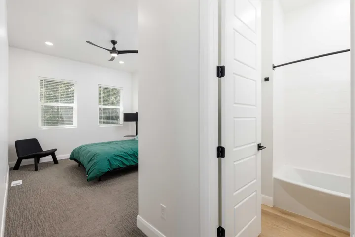 Recessed lighting, ceiling fan, carpeting, paneled interior door with matte black hardware, and a tub with tiled surround