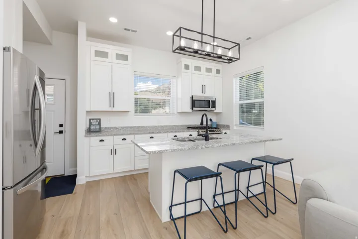 Kitchen featuring white cabinetry, light-toned countertops, a stainless steel appliance suite, an island with seating, and wood-finish flooring
