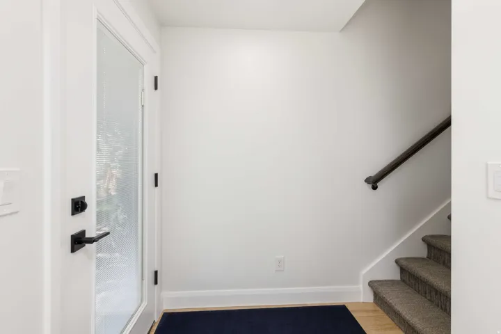 White entry door with frosted glass, black hardware, and wood-finish flooring