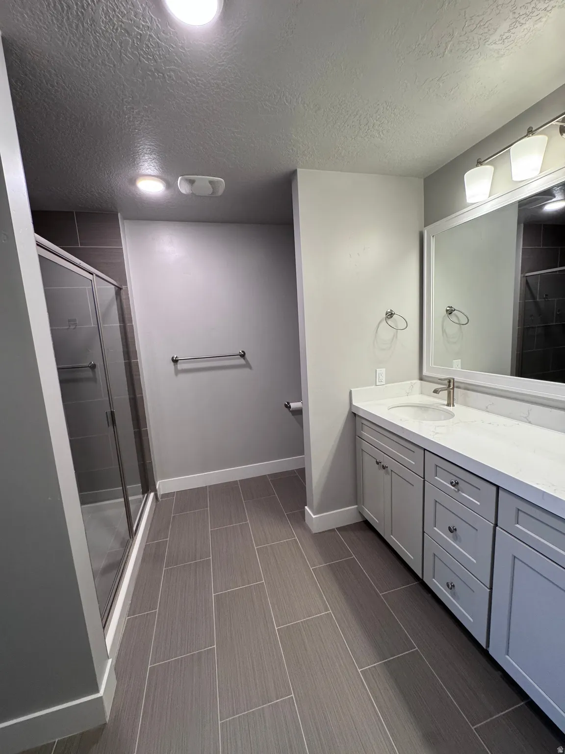 Bathroom featuring a glass-enclosed shower, a double vanity with a light-colored countertop, rectangular floor tiles, and recessed lighting