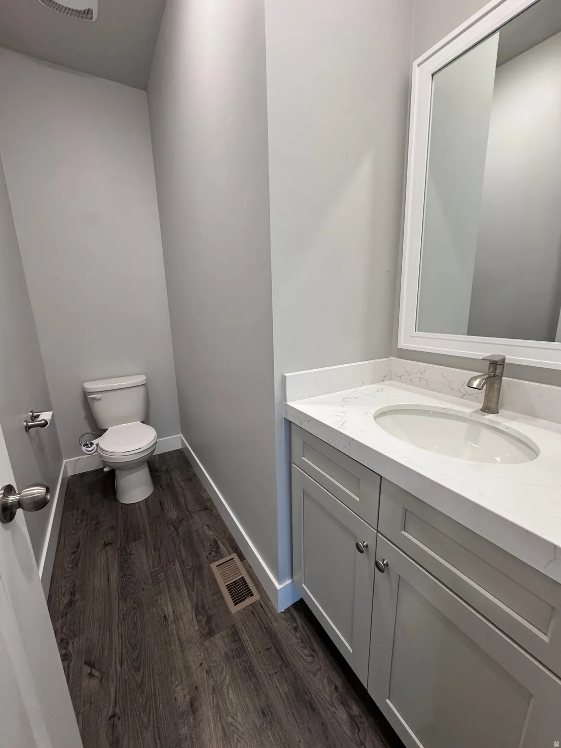 Wood-finish flooring with a light gray vanity, white countertop, and framed mirror