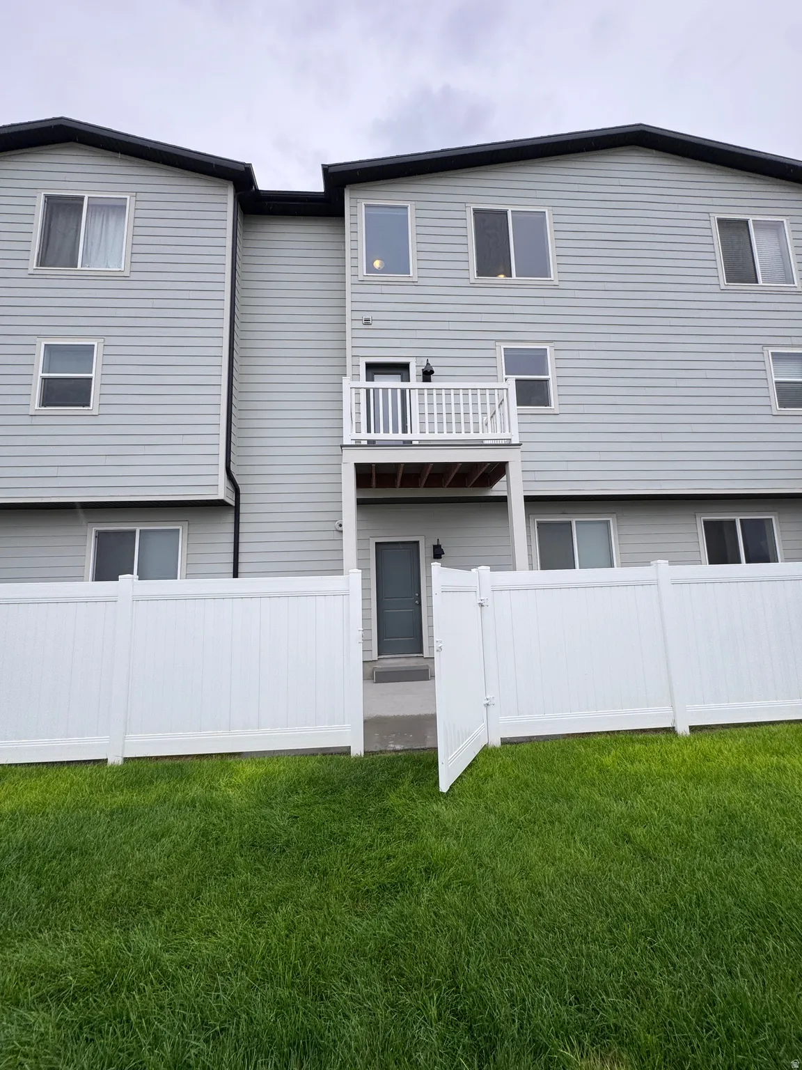 Vinyl siding exterior with multiple windows, private balcony, ground-level entry, and a fenced yard with a gate