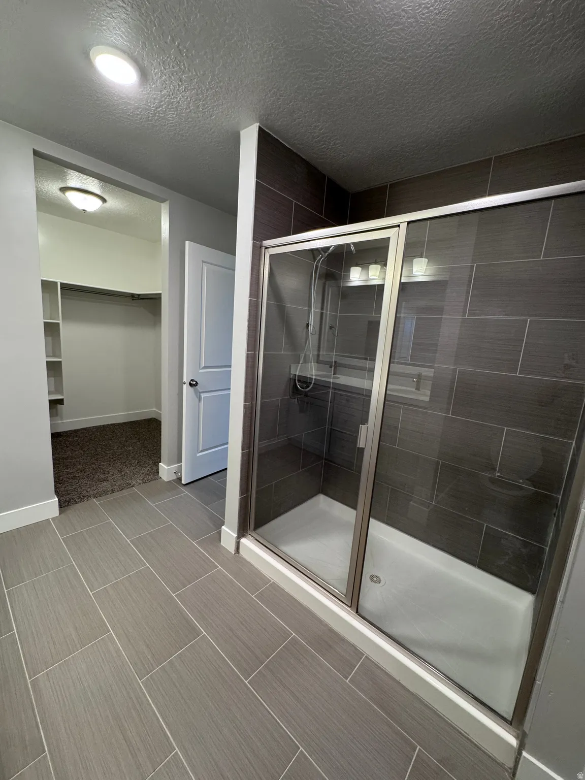 Walk-in shower with dark tile surround and glass enclosure, complemented by large format tile flooring