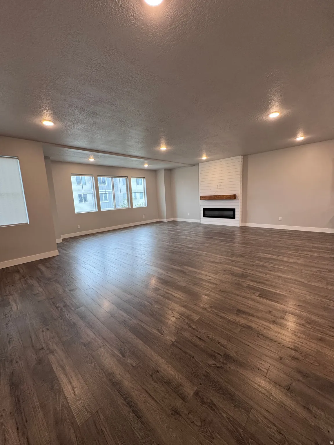 Spacious room featuring wood-finish flooring, recessed lighting, multiple windows, a white brick-textured fireplace, and a wood mantel