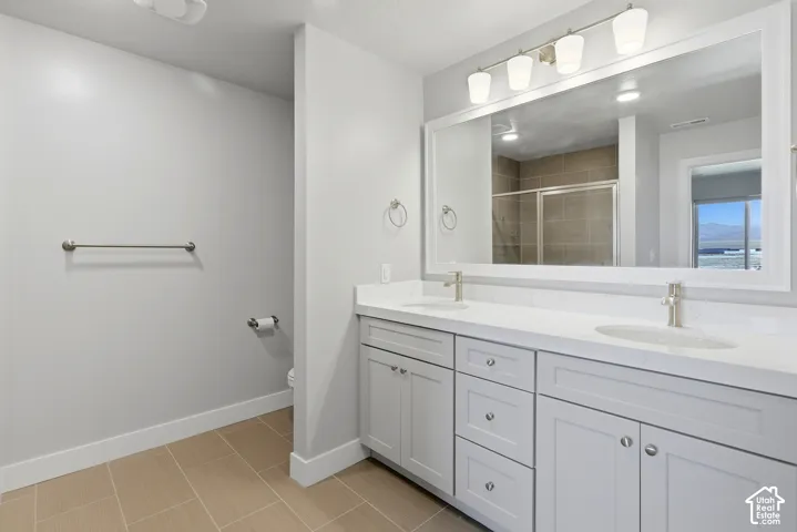 Double vanity with integrated sinks and brushed nickel faucets, light-colored cabinetry, large framed mirror, vanity lighting, and tile flooring