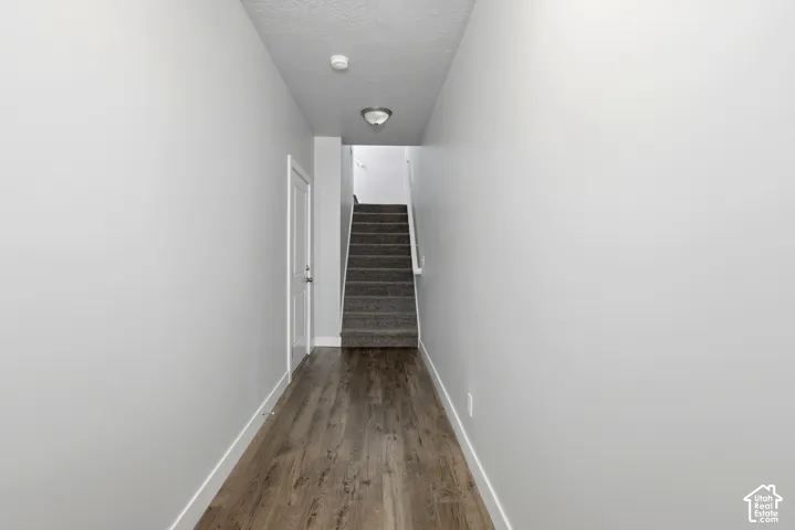 Hallway featuring wood-finish flooring, white walls, and a staircase with carpeted treads