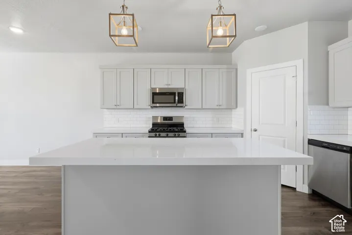 Kitchen featuring light gray cabinetry, white subway tile backsplash, stainless steel appliances, and a central island with a solid surface countertop