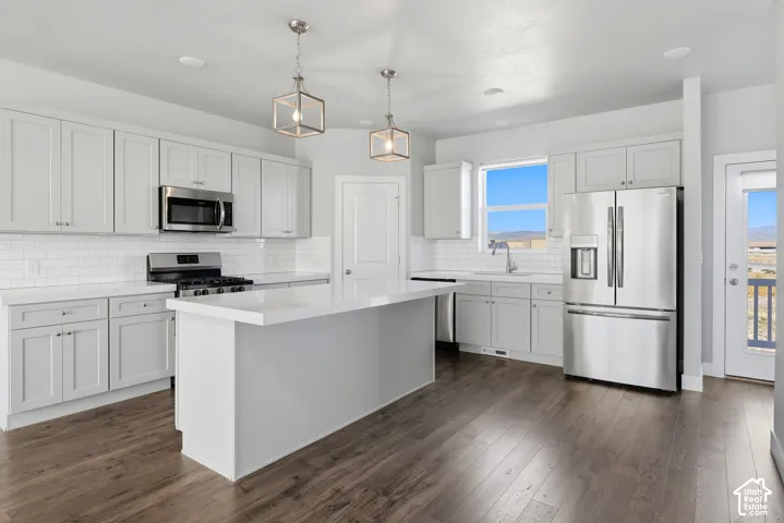 Kitchen featuring wood-finish flooring, white subway tile backsplash, stainless steel appliances, a center island with a white countertop, and pendant lighting