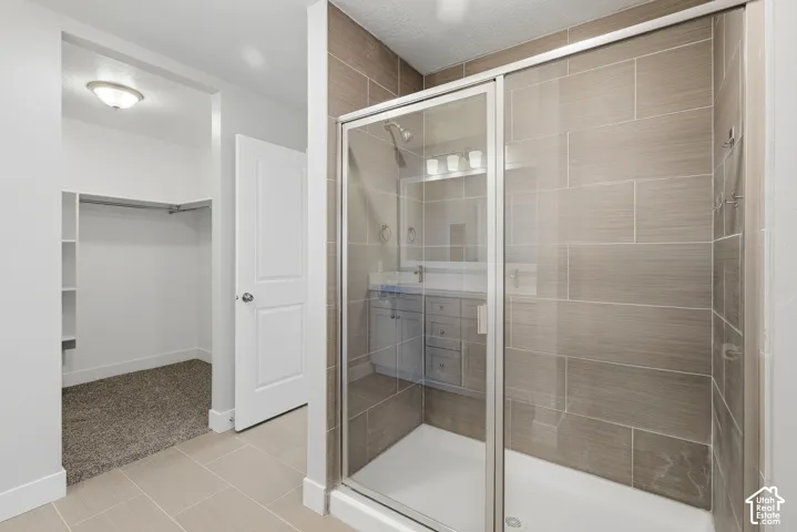 Glass-enclosed shower with horizontal tile surround, single vanity with integrated sink, and a built-in closet with shelving