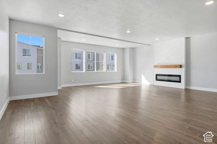 Expansive living area with wood-finish flooring, recessed lighting, multiple windows, and a shiplap-accented fireplace with a wood mantle