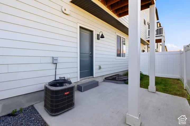 Poured concrete patio with white vinyl fencing, a white siding exterior, and an outdoor wall light fixture