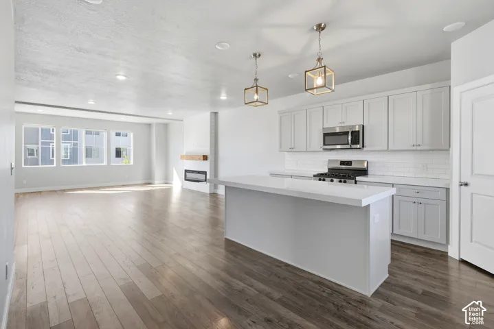 Open-concept living space featuring wood-finish flooring, a modern kitchen island with a white countertop, and light gray cabinetry