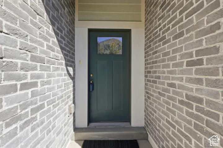 Gray brick exterior featuring a dark green entry door with an upper window pane and white trim