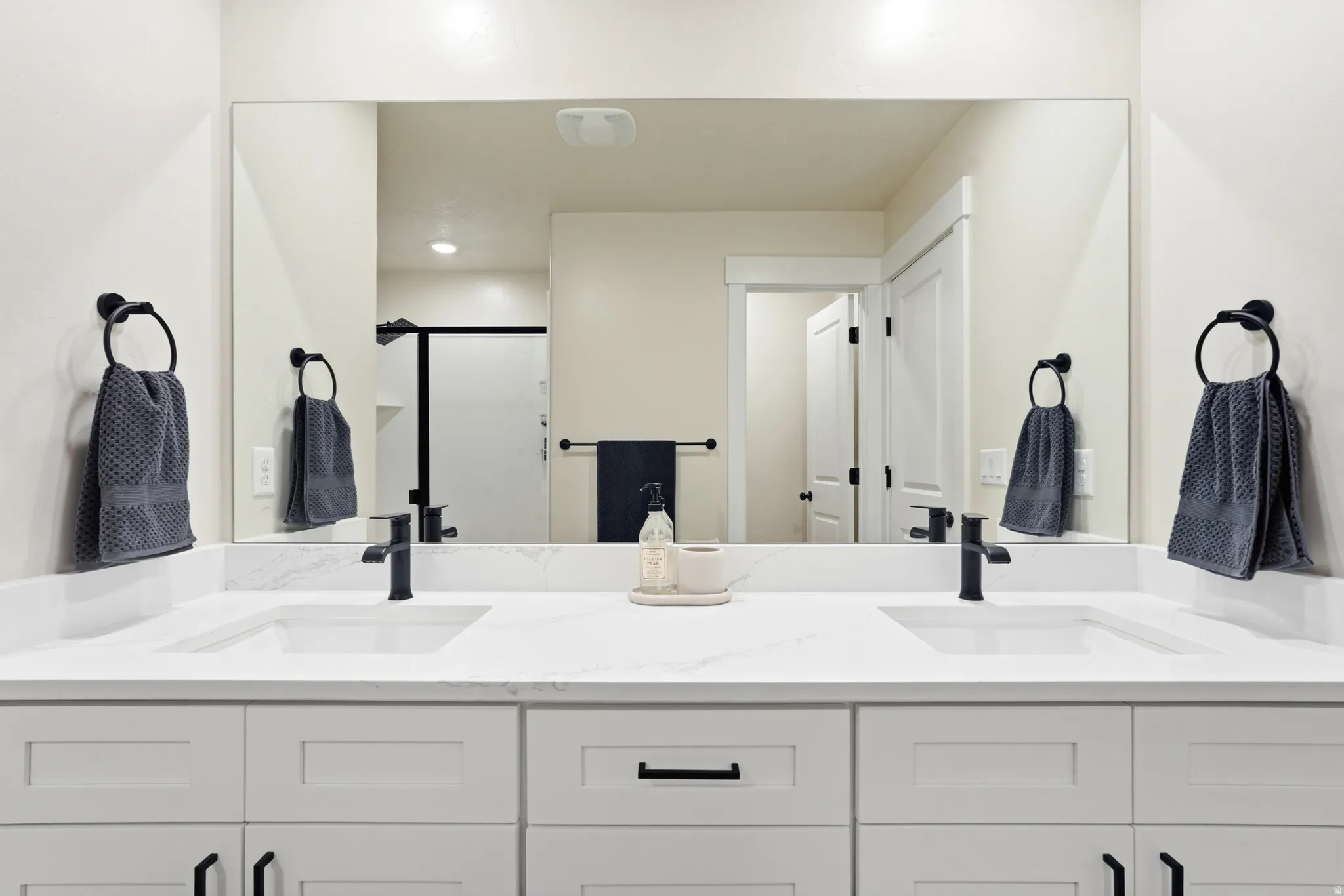 Double vanity with white cabinetry, matte black hardware, integrated sinks, and a large wall-mounted mirror