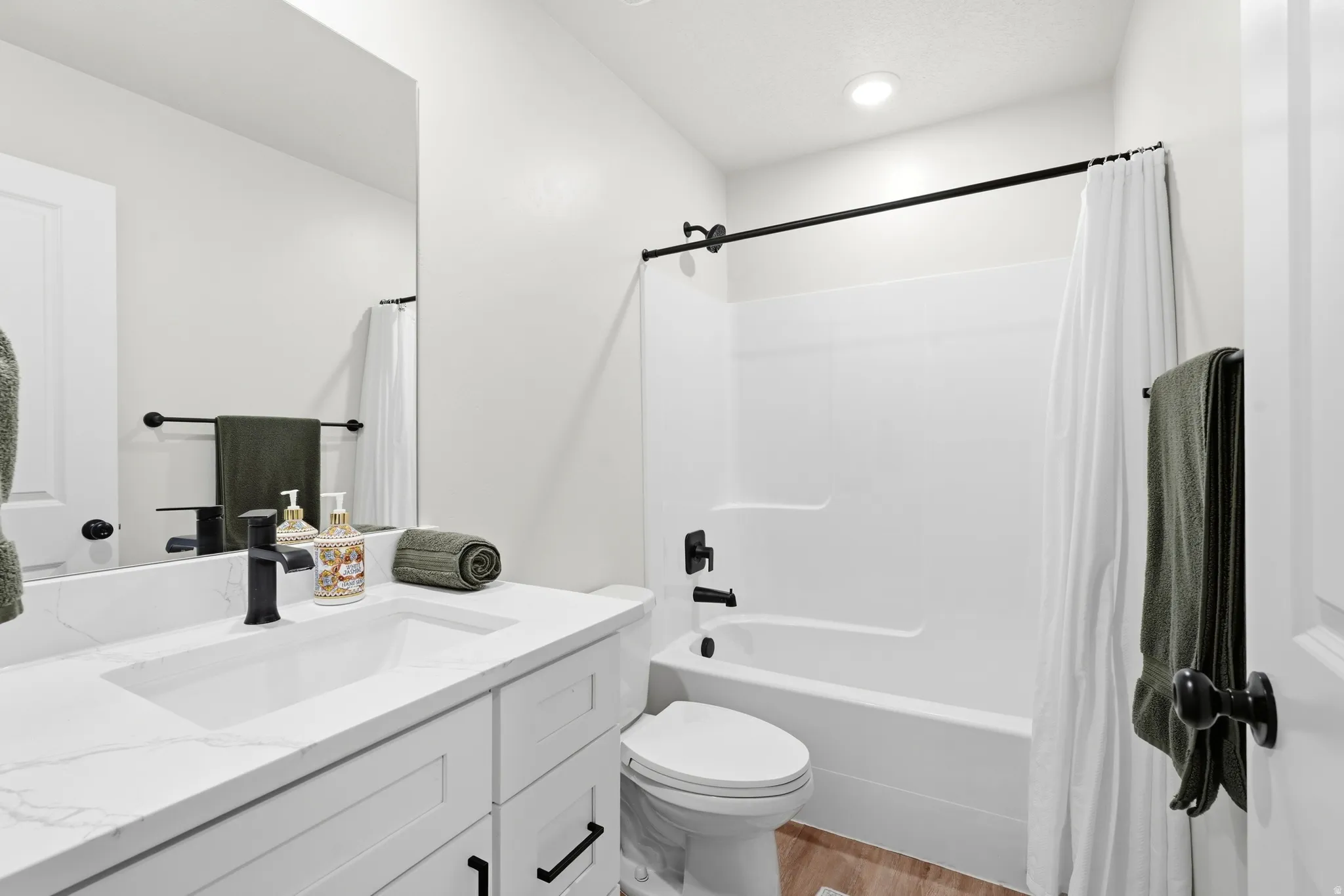 White vanity with a rectangular undermount sink, stone-finish countertop, and black fixtures