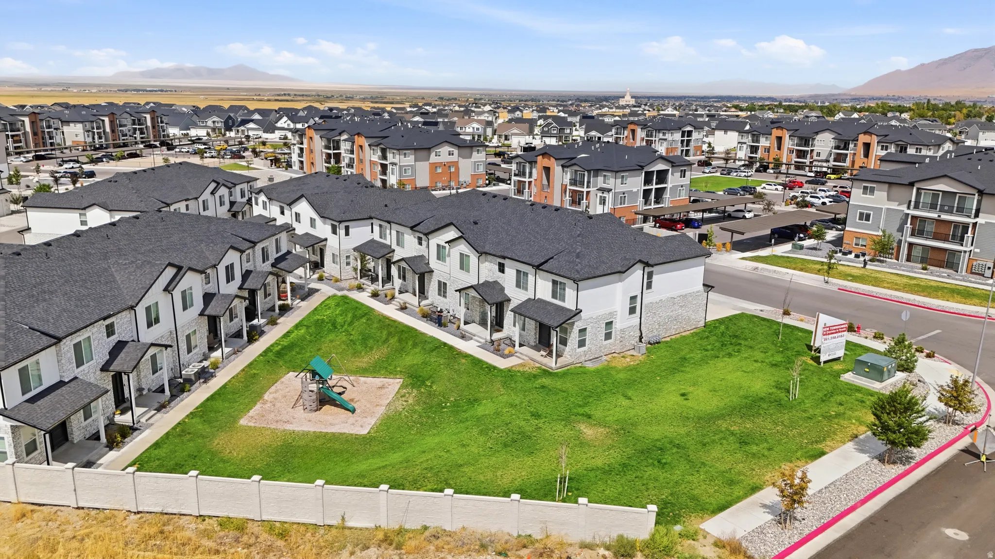 Residential development with multiple townhome-style buildings, green spaces, and mountain backdrop