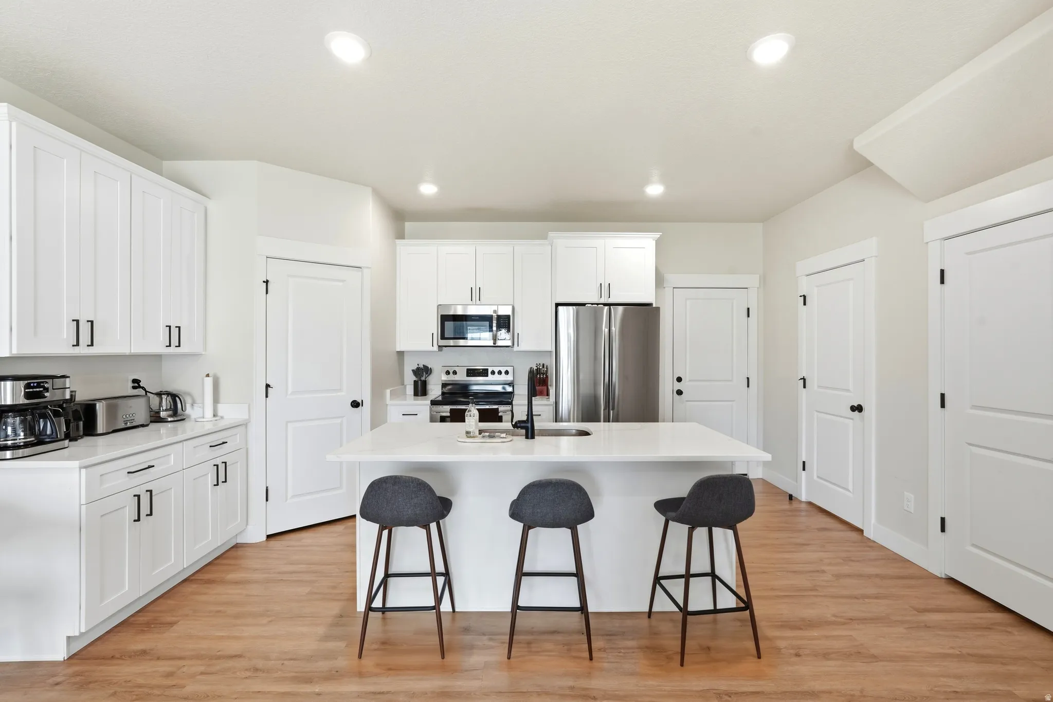 White shaker cabinetry with black hardware, stainless steel appliances, a center island with seating, and wood-finish flooring