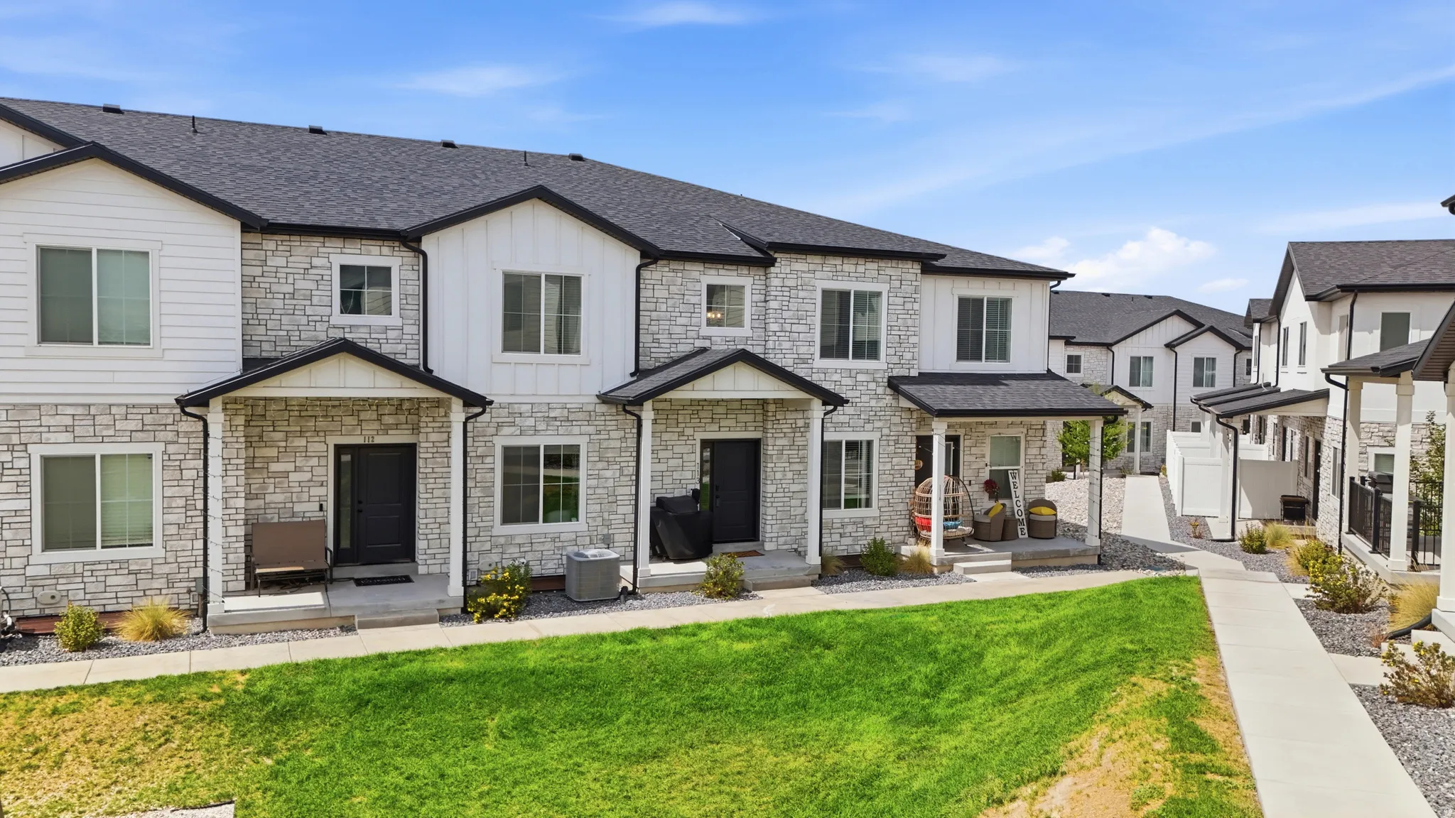 Stone and siding exterior with black window frames, covered entryways, and dark shingle roofing