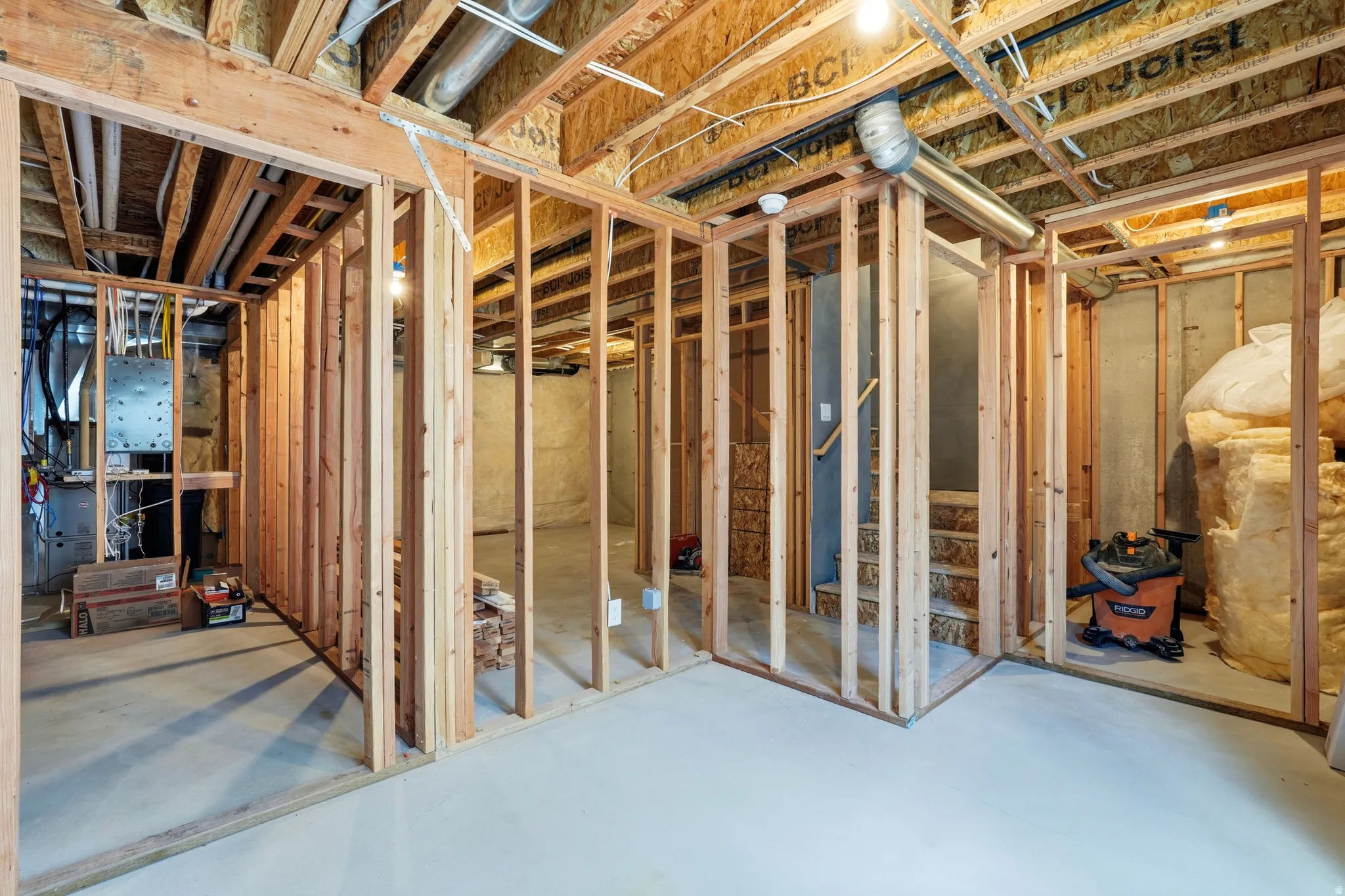 Unfinished basement with concrete flooring, exposed wood framing, and visible utility infrastructure