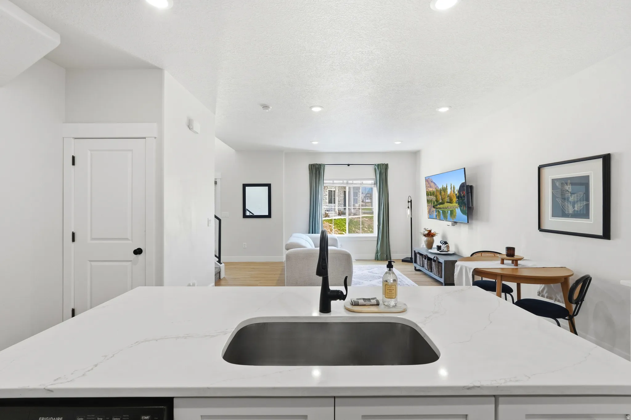 Quartz countertop, undermount sink, black gooseneck faucet, light wood-finish flooring, and recessed lighting
