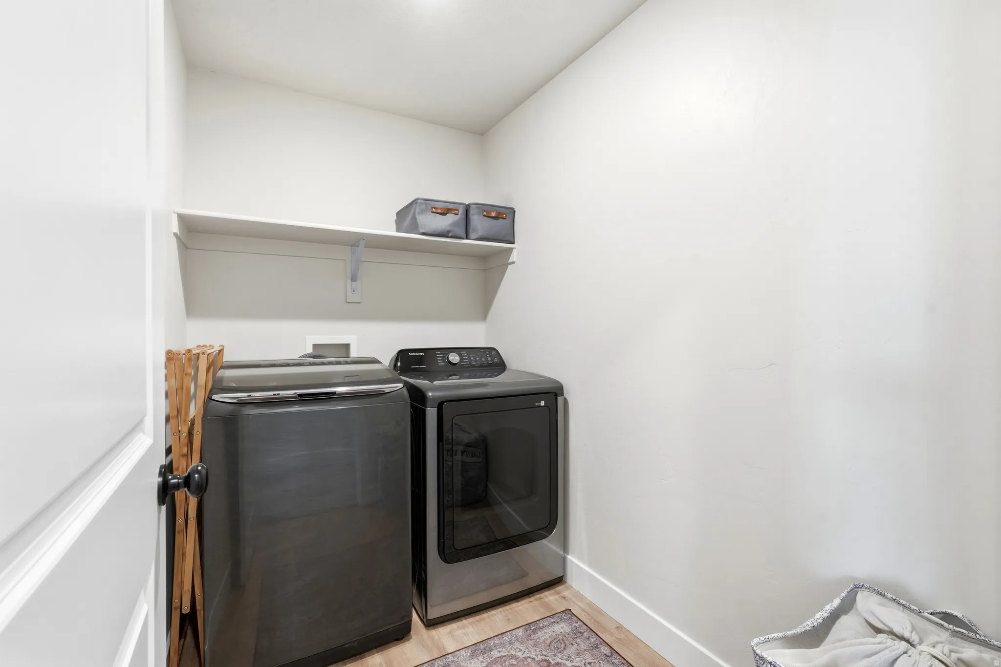 Laundry area featuring a wall-mounted shelf, light-toned walls, and wood-finish flooring
