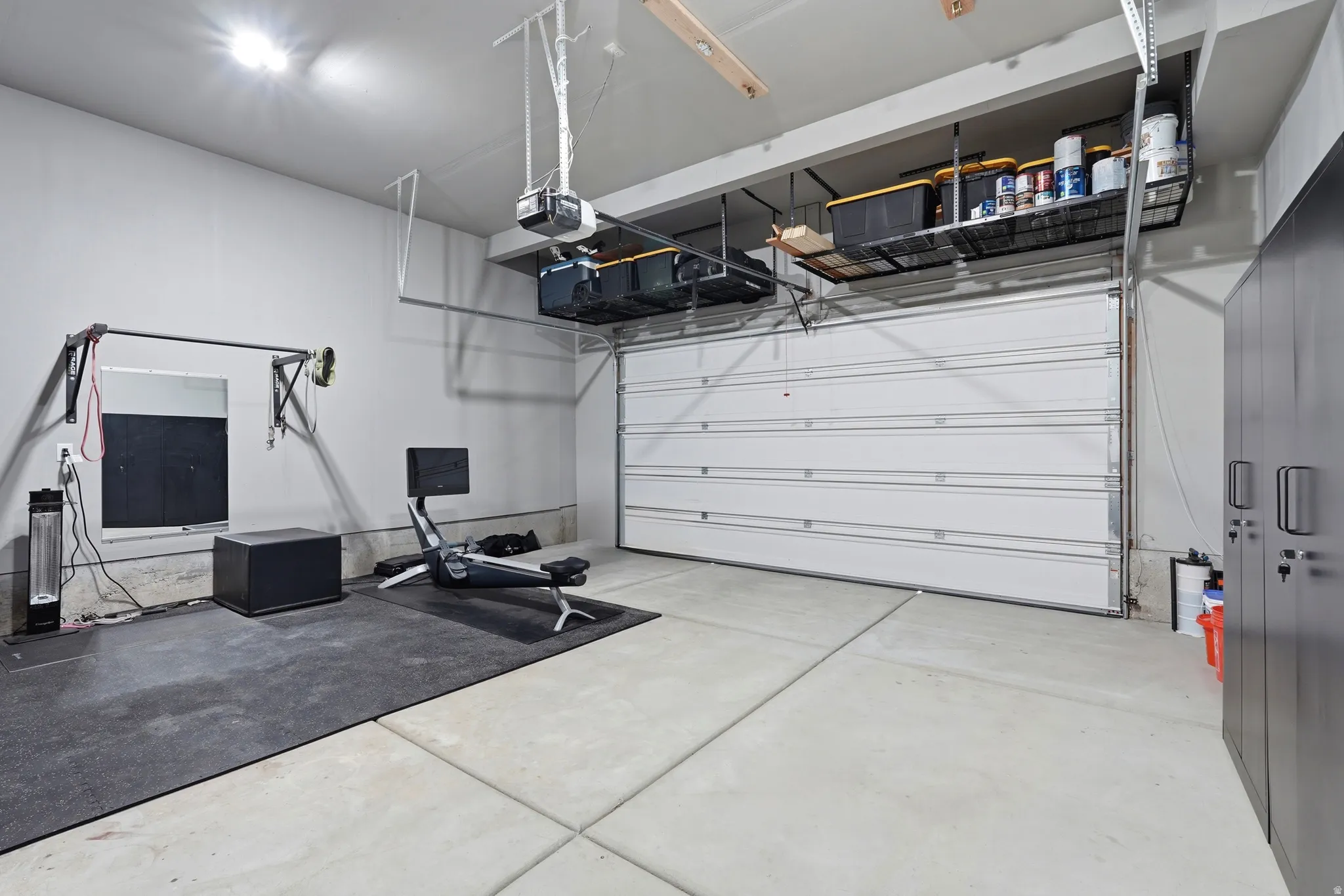 Concrete flooring, bright overhead lighting, built-in overhead storage racks, an automatic garage door opener, and a wall-mounted storage cabinet
