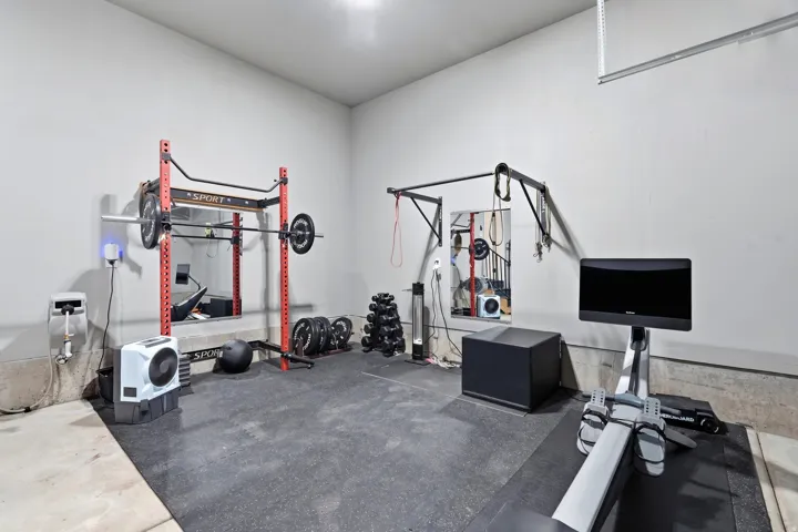 Dedicated fitness area featuring durable rubber flooring, wall-mounted pull-up bar, and specialized power rack with barbell