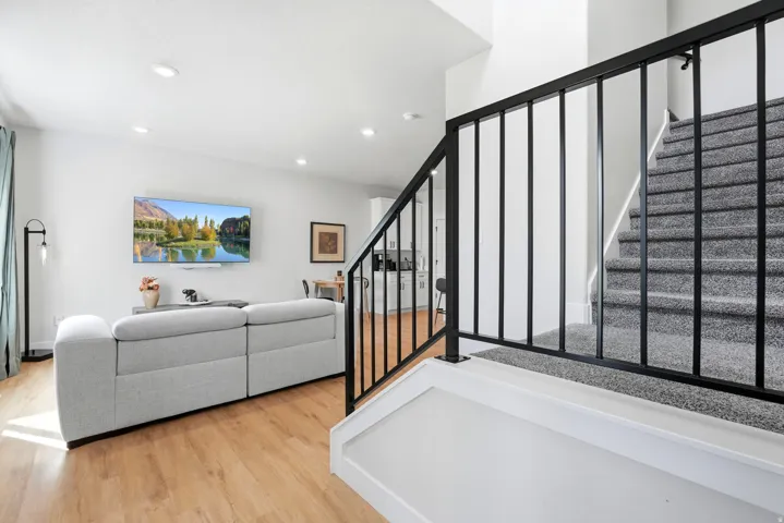 Wood-finish flooring throughout, recessed ceiling lighting, black metal staircase railing, and carpeted stairs