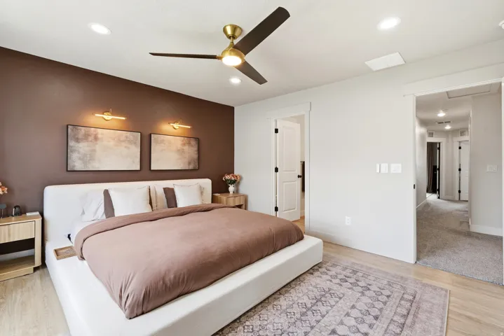 Recessed ceiling lighting, gold-finish ceiling fan, wood-finish flooring, two wall-mounted light fixtures, and a brown accent wall