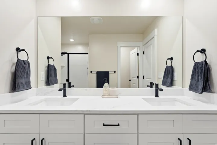 Double vanity with white cabinetry, matte black hardware, integrated sinks, and a large wall-mounted mirror