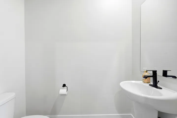 Pedestal sink with a matte black faucet, frameless mirror, and white toilet