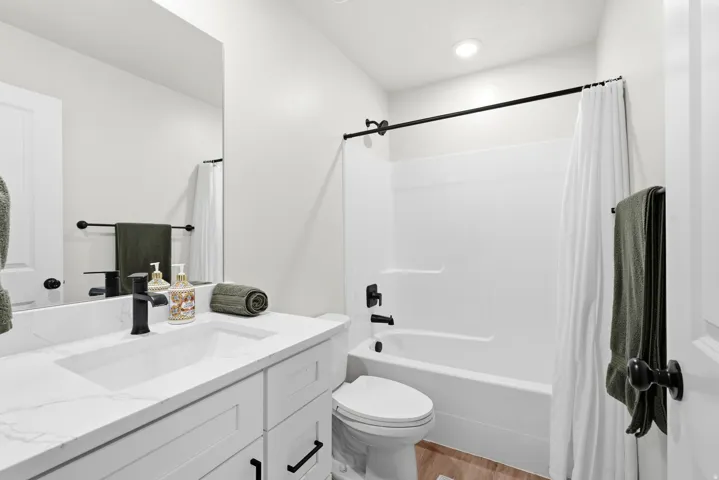 White vanity with a rectangular undermount sink, stone-finish countertop, and black fixtures