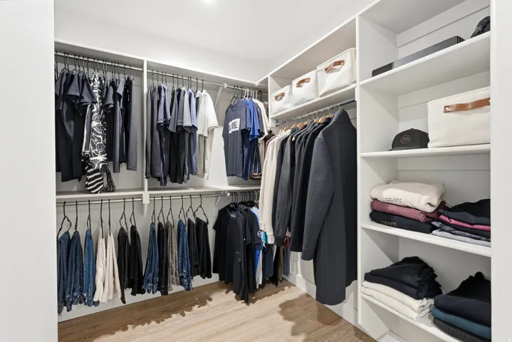 Custom closet system featuring multiple hanging rods, integrated shelving, and wood-finish flooring