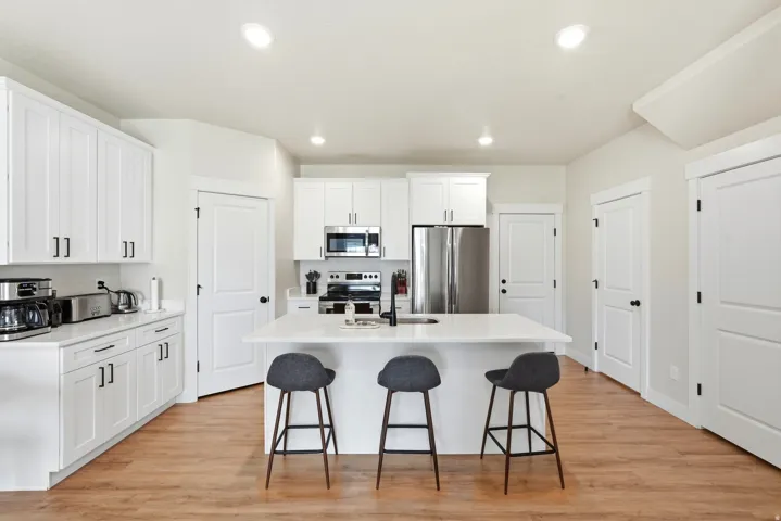 White shaker cabinetry with black hardware, stainless steel appliances, a center island with seating, and wood-finish flooring