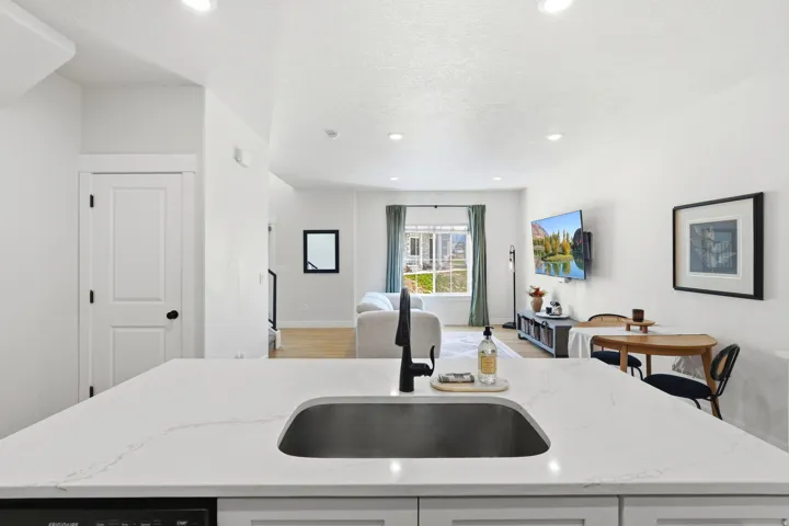 Quartz countertop, undermount sink, black gooseneck faucet, light wood-finish flooring, and recessed lighting